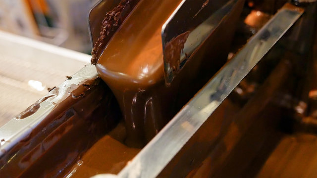 Liquid hot chocolate on the conveyor line of a confectionery factory. Robotics automated chocolate food production. Automatic lines are used instead of human labor on factories and plants.
