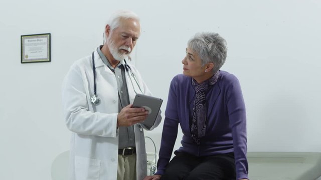 Elderly doctor using tablet to talk to patient