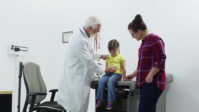 Elderly doctor checking young girl with mother