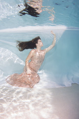 Woman wearing a gown holding her breathe underwater.