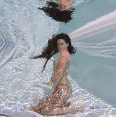 Woman wearing a gown holding her breathe underwater.