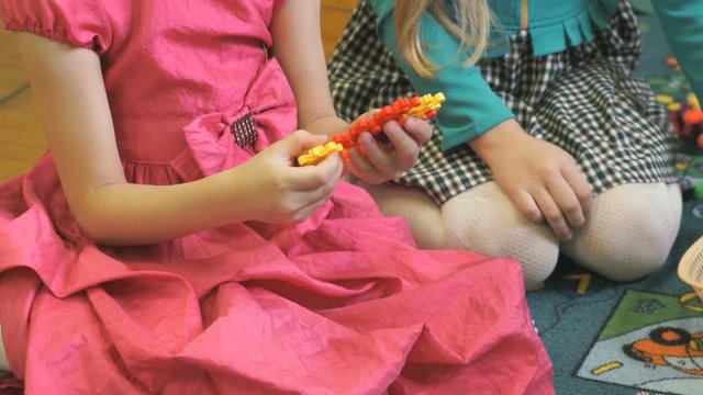 Children play in kindergarten indoors. Close-up of hands of little unidentified girl playing in color designer blocks at table