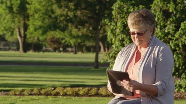 Elderly woman using tablet in the park
