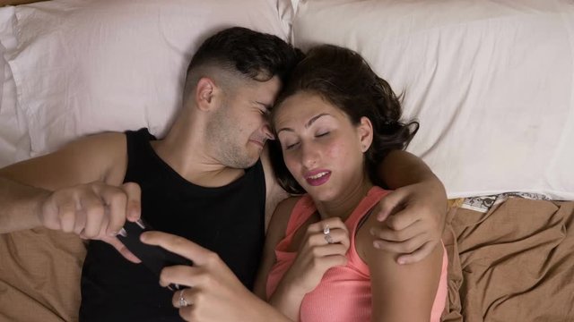 Loving young couple spending time together in bed watching a scary movie on smartphone