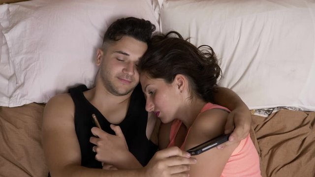 Couple addicted to social media networks spending time in bed together hugging and texting everyone on their smartphones
