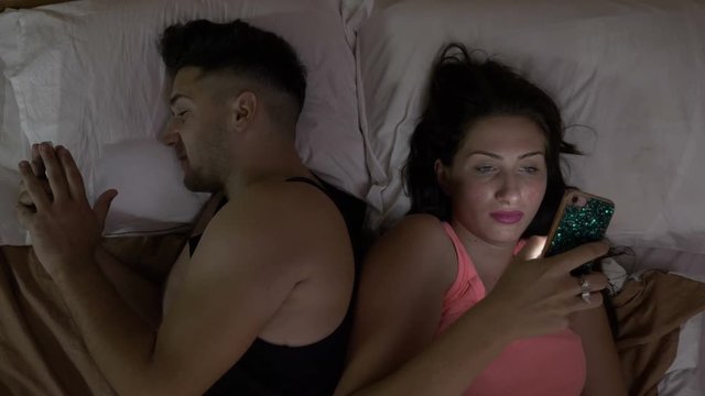 Two lovers sitting in bed at night and doing a video call with firends