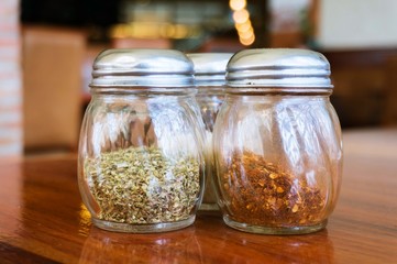 Glass of cheese salt and pepper shakers on wooden table in restaurant