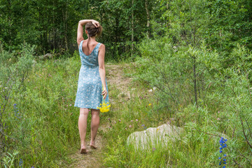 Young woman in romantic blue dress with yellow flowers in the mountains
