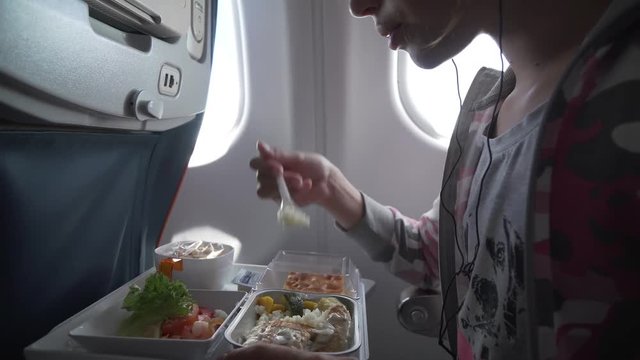 Young girl in the headphones is eating delicious dinner on the airplane stock footage video