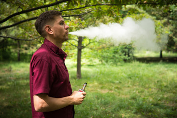 Vape man. Young man is smoking an electronic cigarette at the summer park