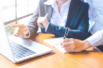 Two business women working in a notebook computer and writing on a notebook with a pen.