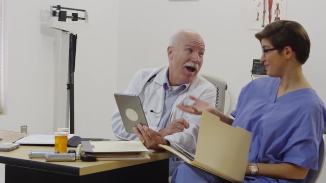 Elderly doctor and nurse discussing using tablet and taking notes