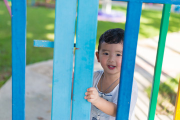 Obraz premium Smile Asian kid behind the colorful fence at playground in summer. shallow DOF.