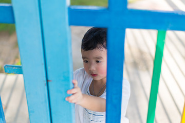 Sad Asian kid behind the grid trying to escape. shallow DOF