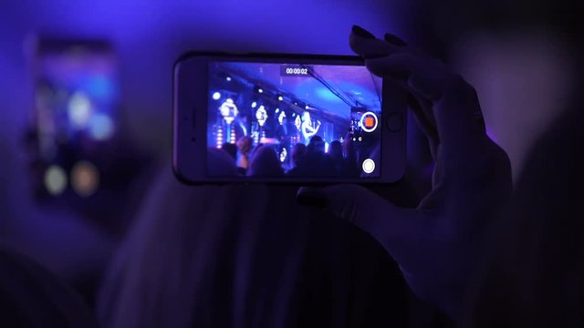 The presentation of new collection young designers in privat area indoors of nightclub. Crowded hall is wathing perform and record the video at telephone hold in hand horizontal, floodlight flashing