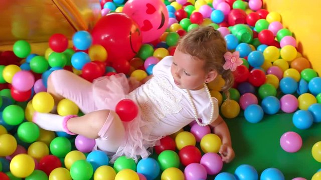 Little girl 4-5 years crawling around in the large pool with plastic balls, slow motion.