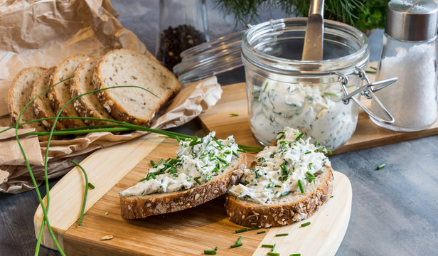 Home made bread on a wooden cutting board with curd cheese and ricotta and herbs. Decorated with green herbs 