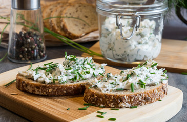 Home made bread on a wooden cutting board with curd cheese and ricotta and herbs. Decorated with green herbs 