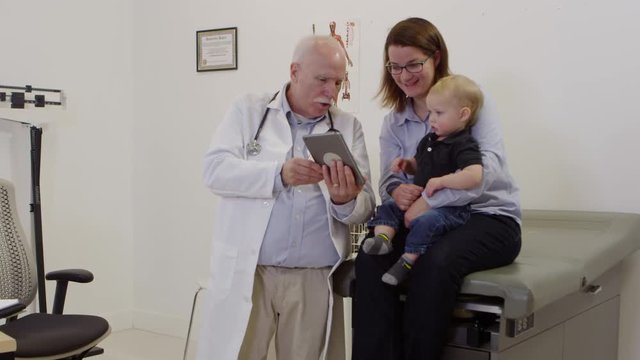 Elderly doctor using tablet to speak to mother and baby patient