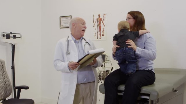 Elderly doctor checking out baby and talking to mother