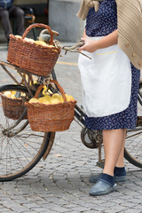 Asti, Italy - September 10, 2017: Woman dressed in antique clothes carries yellow peach baskets on an old bicycle