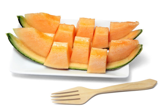 Sliced orange melon in pieces on a white plate with wooden fork on white background.