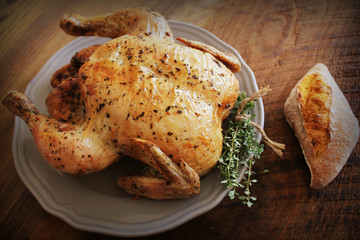 Whole roasted chicken with thyme and bread on wooden background