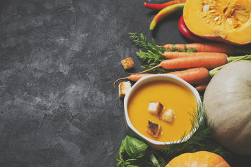 Creamy pumpkins soup with vegetables over black texture