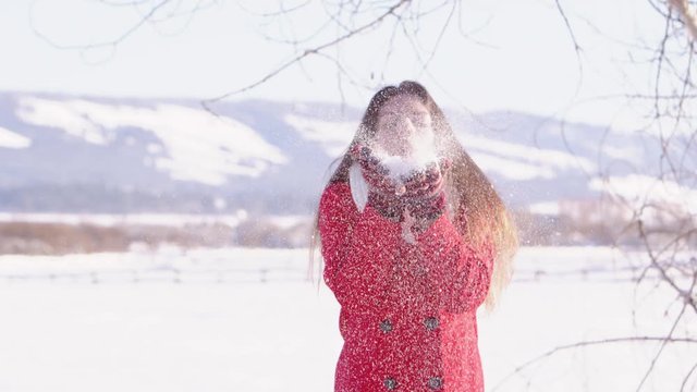Slow motiong young woman blowing snow off of her gloves