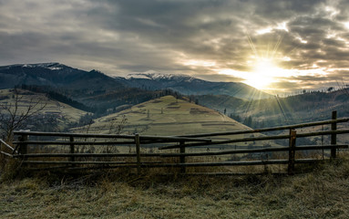 fence on hillside in late autumn gloomy sunrise. high mountain ridge with snowy tops in a distance under overcast sky