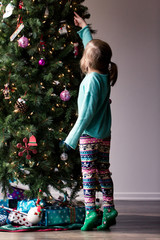 A young girl with is decorating a Christmas tree and is happily playing with the decorations.