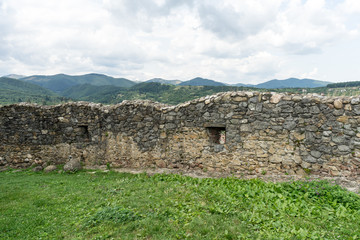 Old ruined stone wall of ancient Cisnadioara fortress in Sibiu, Romania. Green grass all around. Mountains in background.