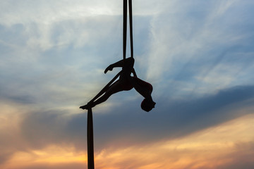 Woman in a hammock does tricks against the sky, she is an athlete aerial acrobat.