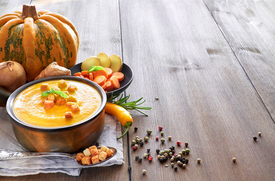 Pumpkin, carrot and ginger creme soup in ceramic pan on the wooden table