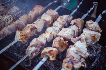 Grilled kebab cooking on metal skewers (grill). Roasted meat cooked at barbecue with smoke. Close up BBQ fresh pork meat chop slices. Traditional eastern dish, shish kebab.
