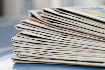 Time to read concept. Newspapers folded and stacked on the blue surface and blur background. Closeup, selective focus