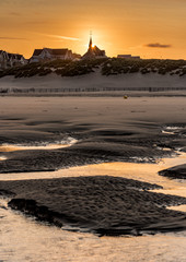 The sun rises behind the church and the buildings of the coast on the beach of Berk and its pools of water left by the low tide.