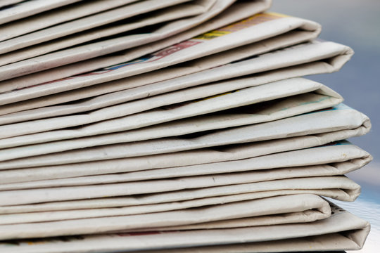 Time to read concept. Newspapers folded and stacked on the blue surface and blur background. Closeup, selective focus