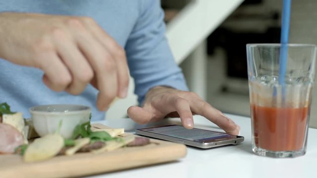Man eating lunch and reading news on smartphone

