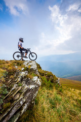 A man stands with a bike on top of the mountain.