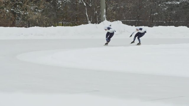 Slow motion of professional speed skaters in sportswear racing along track in outdoor ice rink