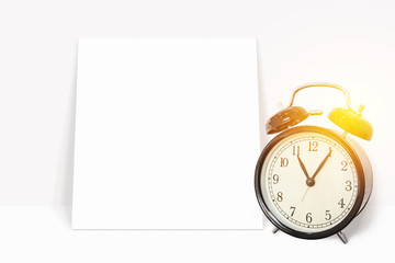 time management concept. analog vintage black clock with blank white paper leaning against the...