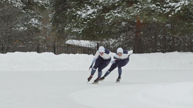 Slow motion of female speed skaters racing along track of outdoor ice rink in winter
