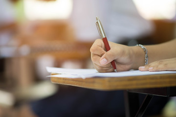 Closeup to hand of student  holding pen and taking exam in classroom with stress for education test...