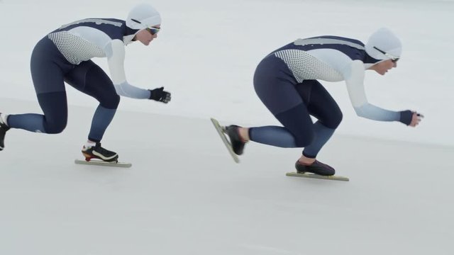 Tracking With Slow Motion Of Professional Female Speed Skaters Wearing Spandex Full-body Covering Suits Sprinting Along Track In Ice Rink