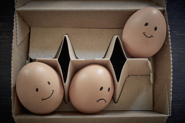 Drei Eier mit aufgemalten Gesichtern im Karton