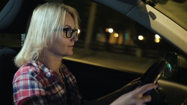 A woman in glasses drives a car through the night city