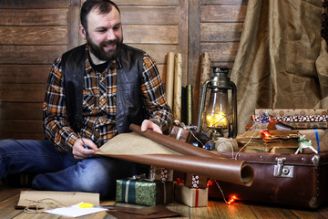 bearded man in shirt and vest packs Christmas gifts posing at camera