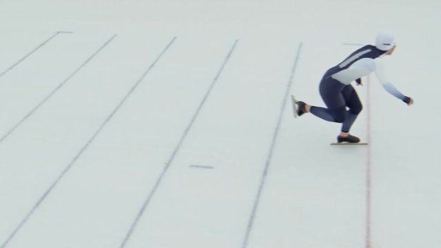High angle shot with slow motion of female speed skater in spandex full-body covering suit and protective eyewear racing on ice during practice