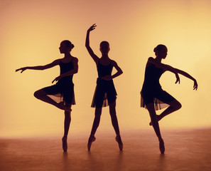 Composition from silhouettes of three young dancers in ballet poses on a orange background.